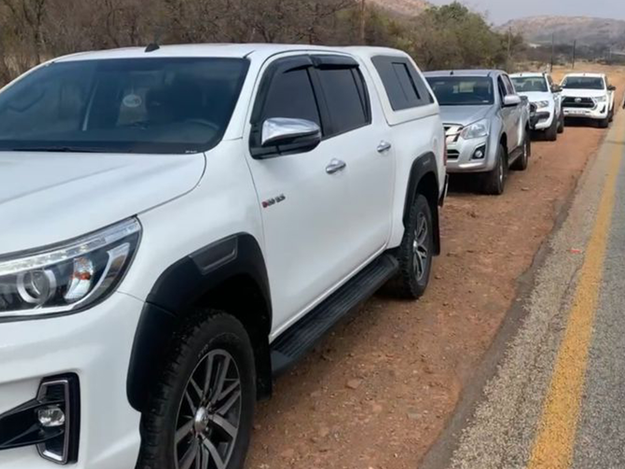Several Toyota Hilux 4x4 trucks lined up against a backdrop of South African terrain