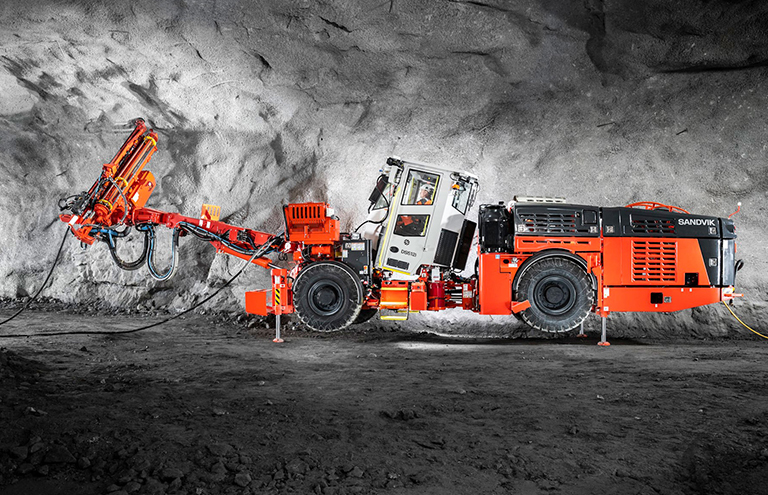 Orange bolting drill rig in an underground cave, drilling in the cave roof